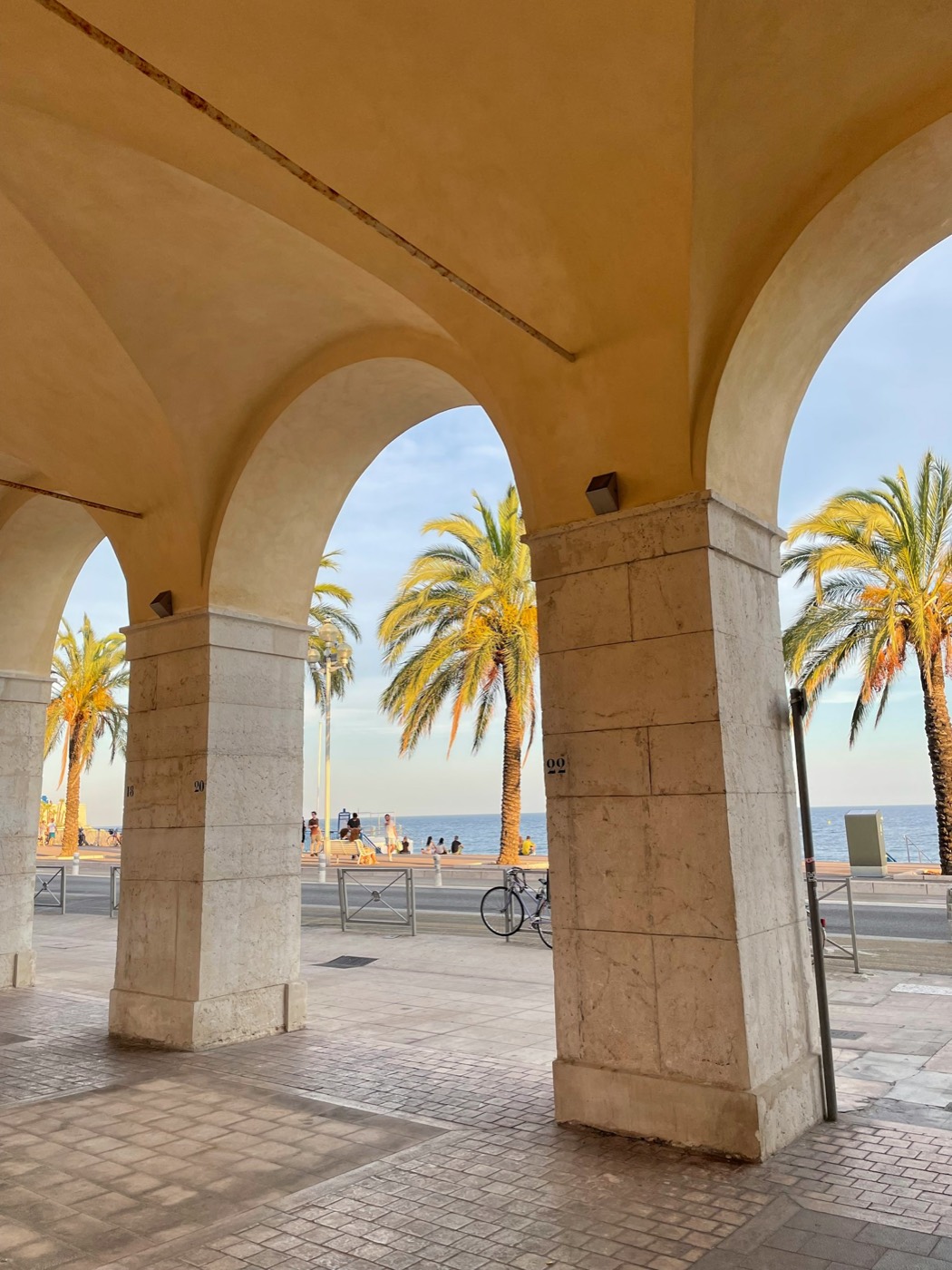 Les arcades de la Promenade des Anglais à Nice, palmiers et mer dans la lumière du soir